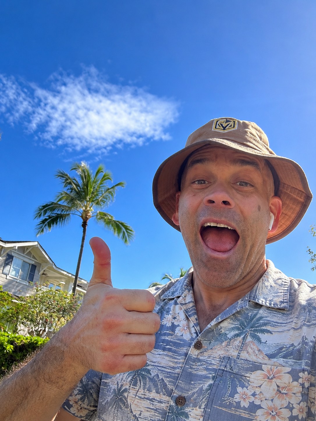 John smiling outdoors in his bucket hat and Hawaiian shirt, giving a thumbs-up